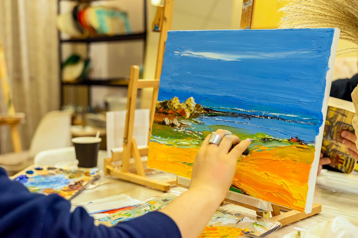 Hand painting colorful scenic seascape landscape on canvas using palette knife in cozy art studio environment